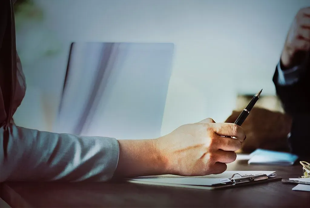Personne rédigeant un document avec un stylo lors d'un entretien.