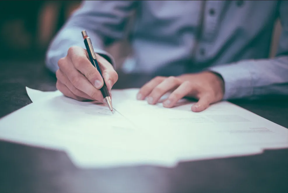 Main d'une personne écrivant au stylo sur des documents officiels.